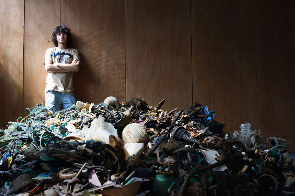 Boyan Slat standing behind a pile of plastic garbage. The plastic was collected by volunteers in Hawaii. Photo courtesy of The Ocean Clean Up