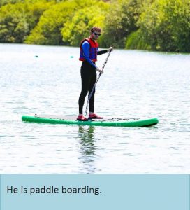 A man standing on a paddleboard. Caption reads he is paddleboarding.